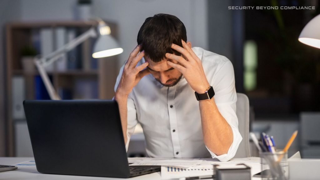 The image shows a man leaning over a desk in dismay that they have been phished. 
